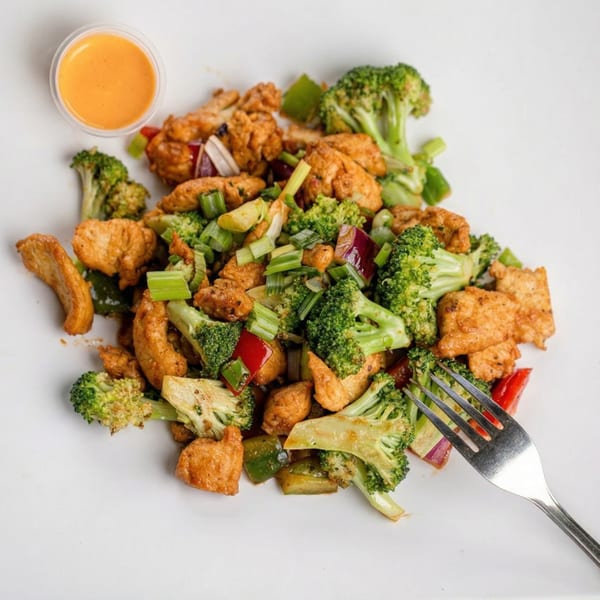 Chicken stir-fry with broccoli, bell peppers, and green onions, served with a side of sauce.