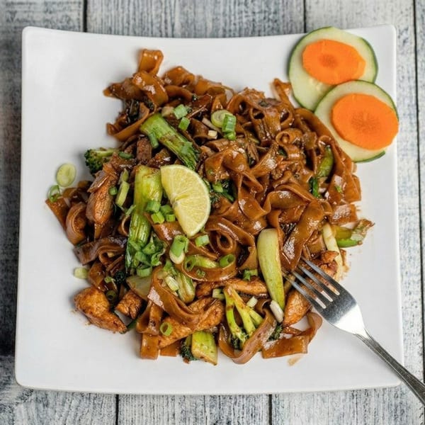 Pad See Ew with chicken, broccoli, green onions, and a lime wedge on a white plate.