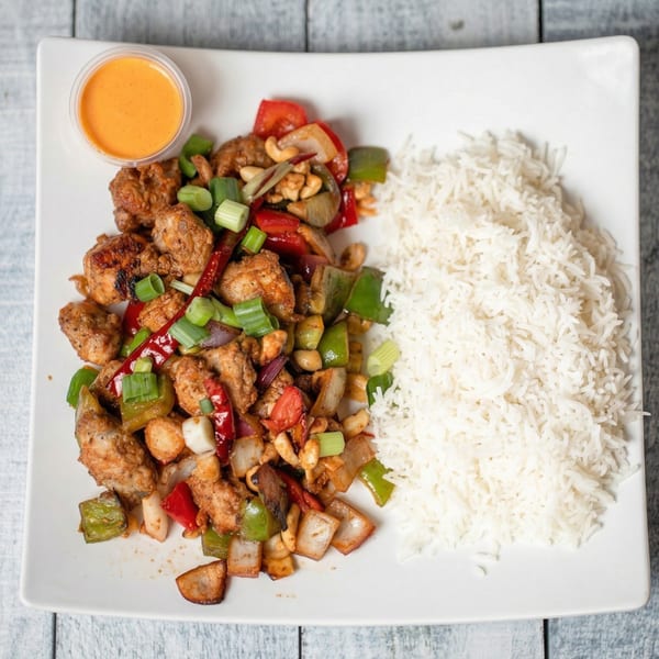 Kung Pao chicken with cashews, bell peppers, and green onions, served with white rice and sauce.